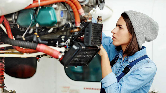 Eine junge Frau werkelt an einem Motor. 